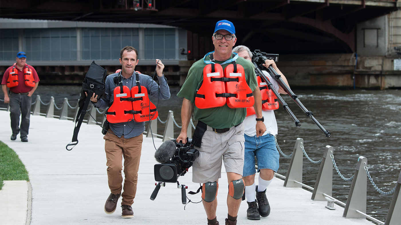 The crew walks along the Chicago River before filming an interview aboard a tugboat