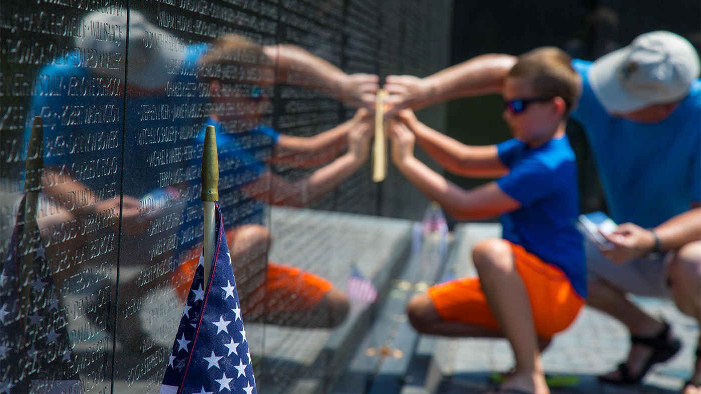 Two visitors make a rubbing of a name of a dead or missing soldier at the Vietnam Veterans Memorial in Washington, D.C.