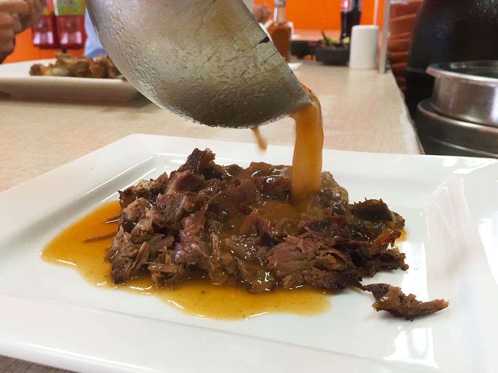 Ladling a consomme over the birria
