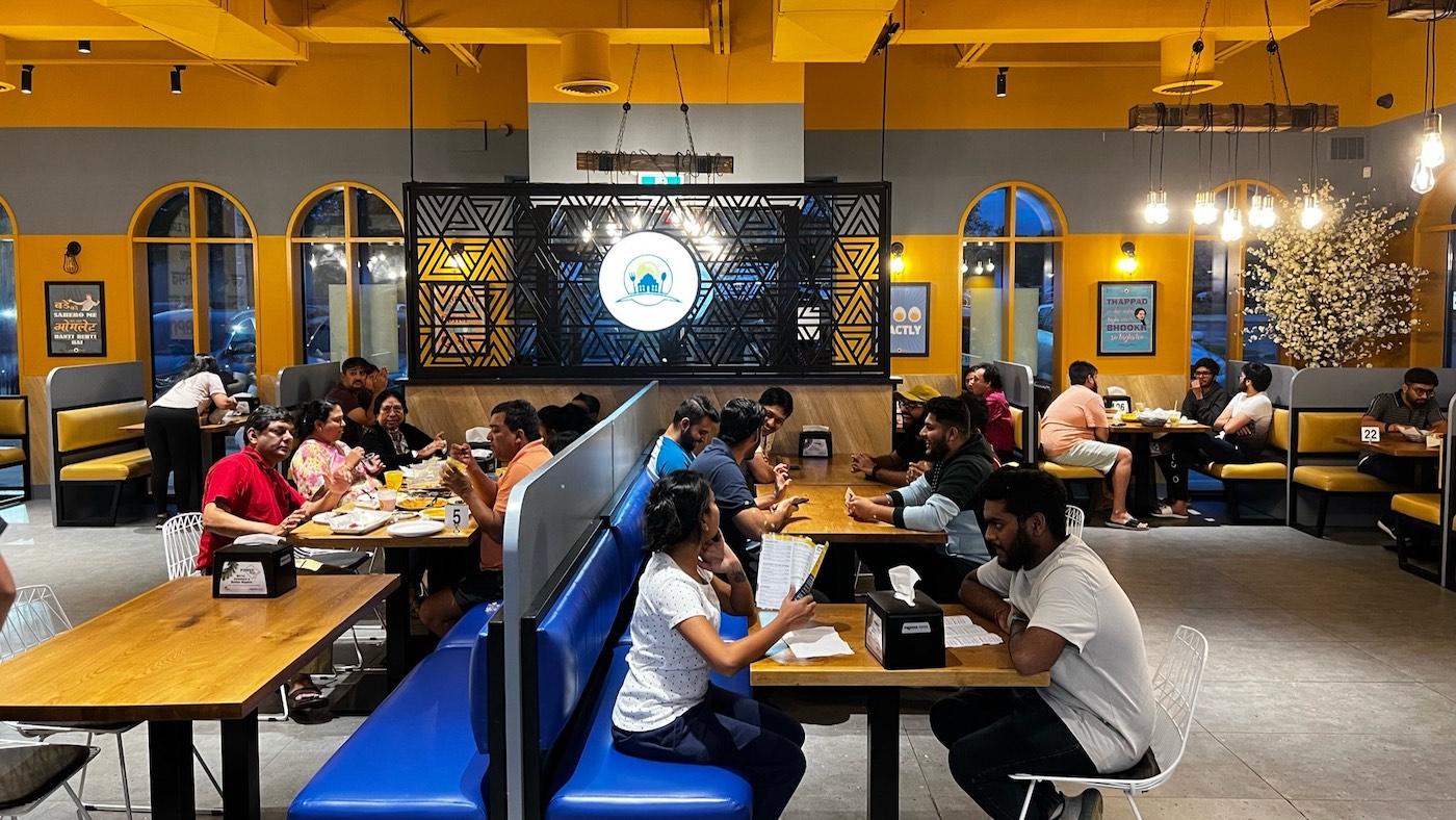 The interior of an Eggholic restaurant, with a yellow and blue color scheme and people eating at tables