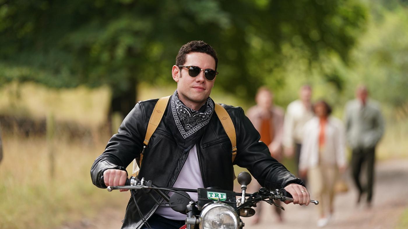 Will Davenport wearing sunglasses and a leather jacket and bandanna on his motorcycle