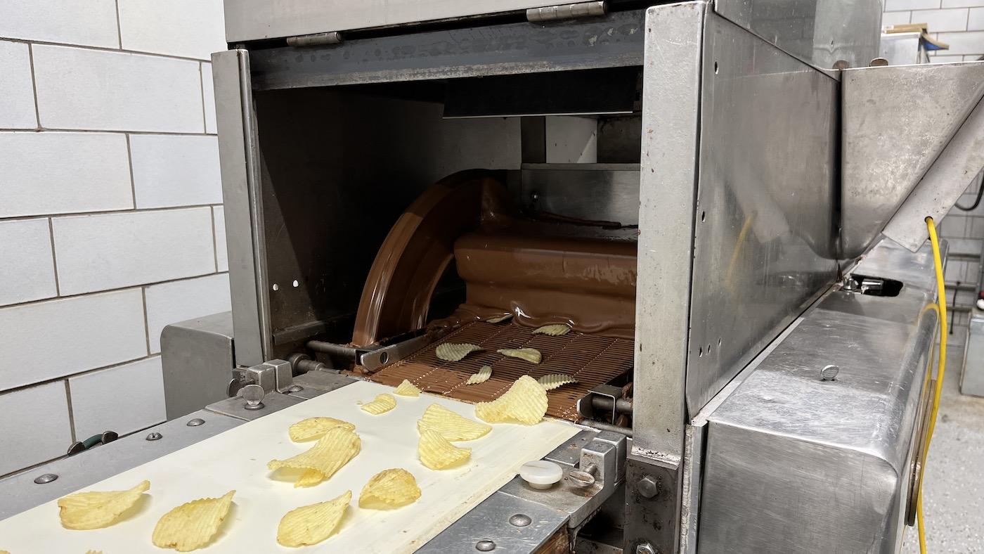 Potato chips on a conveyor belt going through a curtain of liquid chocolate 