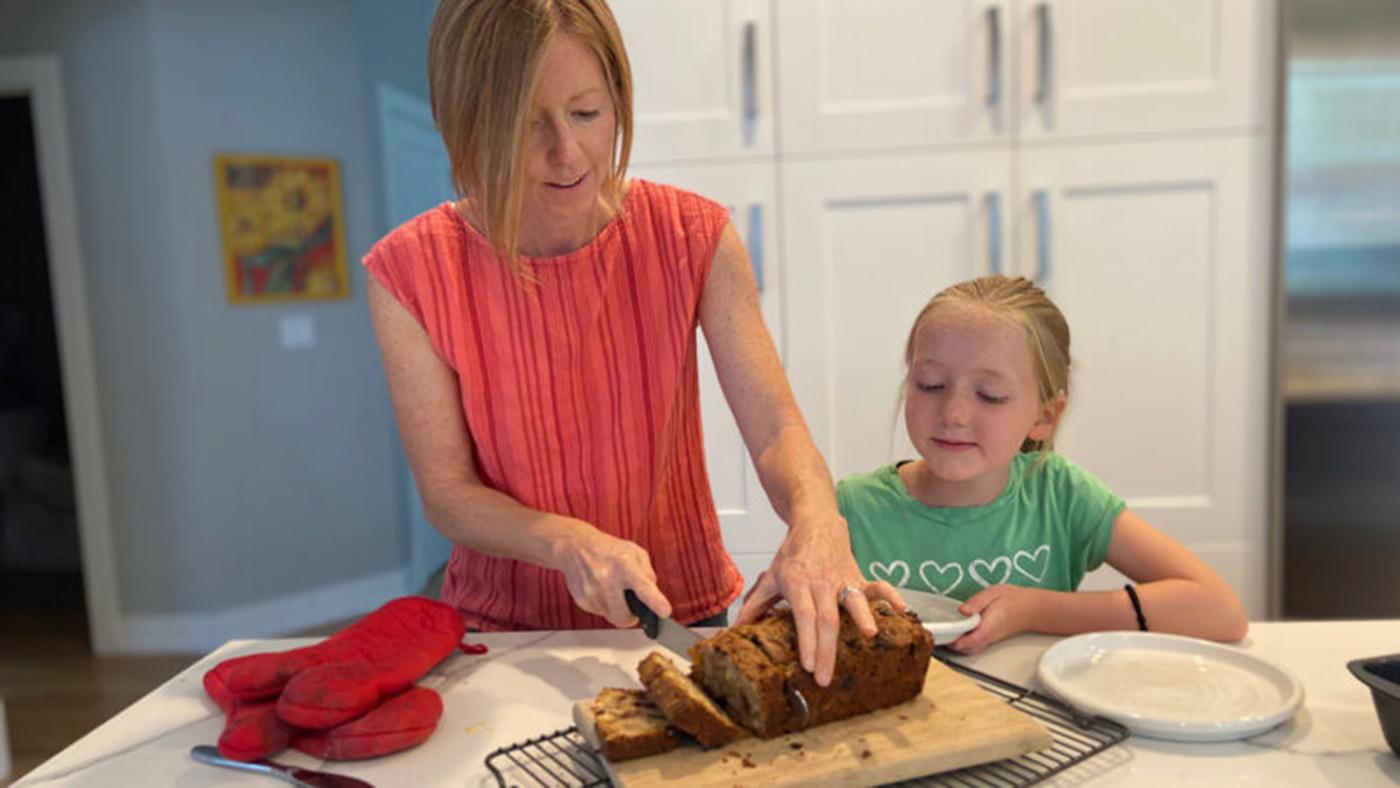 A mother and daughter slice a fruitcake together