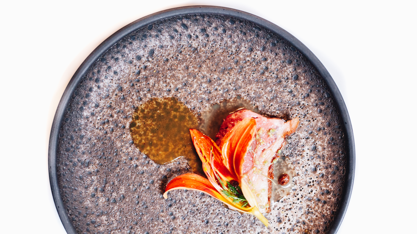 A pebbled plate with an artfully plated dish featuring a flower and sauce
