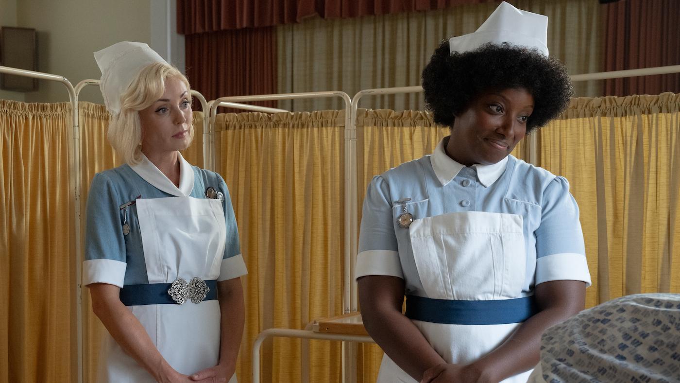 Trixie and Joyce stand in nurse's uniform in front of a patient