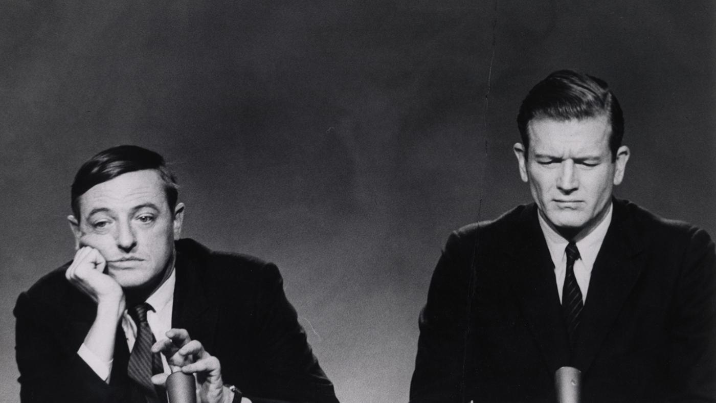 William Buckley looks bored behind a mic while John Lindsay looks annoyed next to him