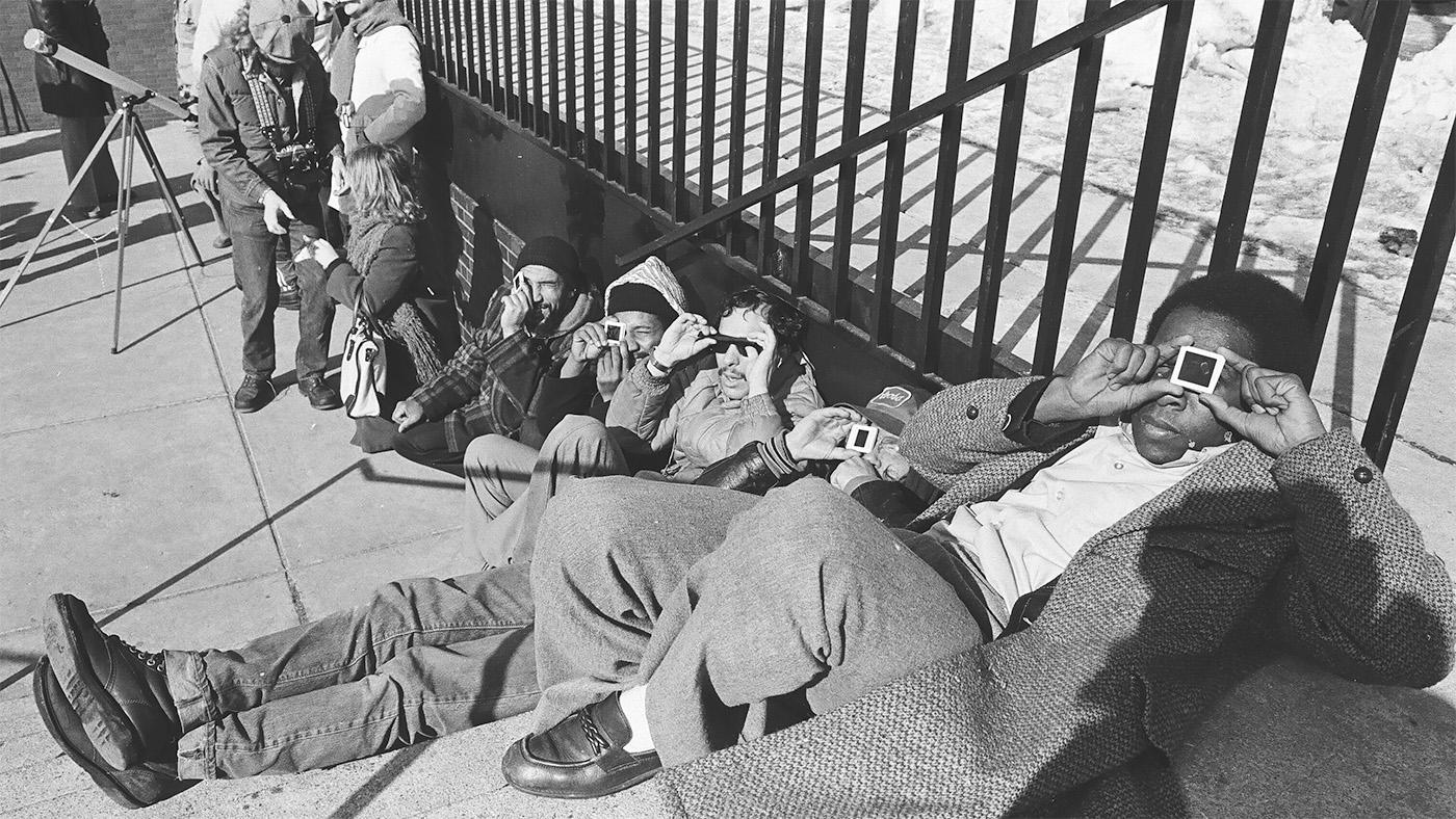 A black and white image of eclipse viewers sitting on the ground and viewing the eclipse through viewing devices at Adler Planetarium in 1979.