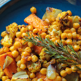 A blue plate of chickpea stew with vegetables and a sprig of rosemary