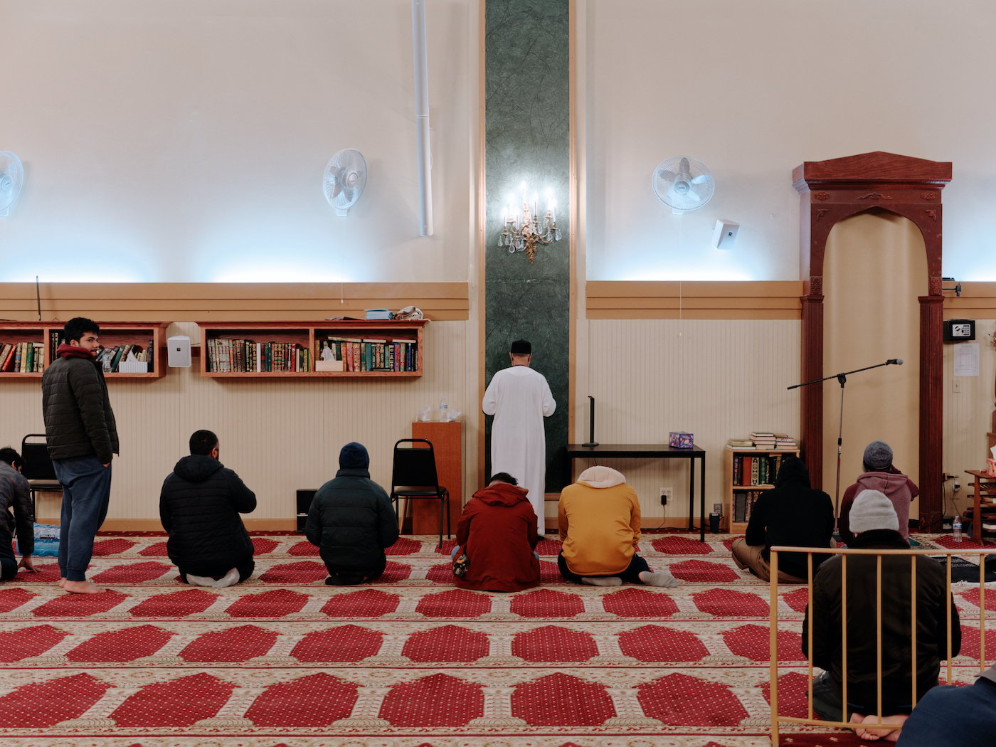 Men stand and sit facing forward in a prayer hall