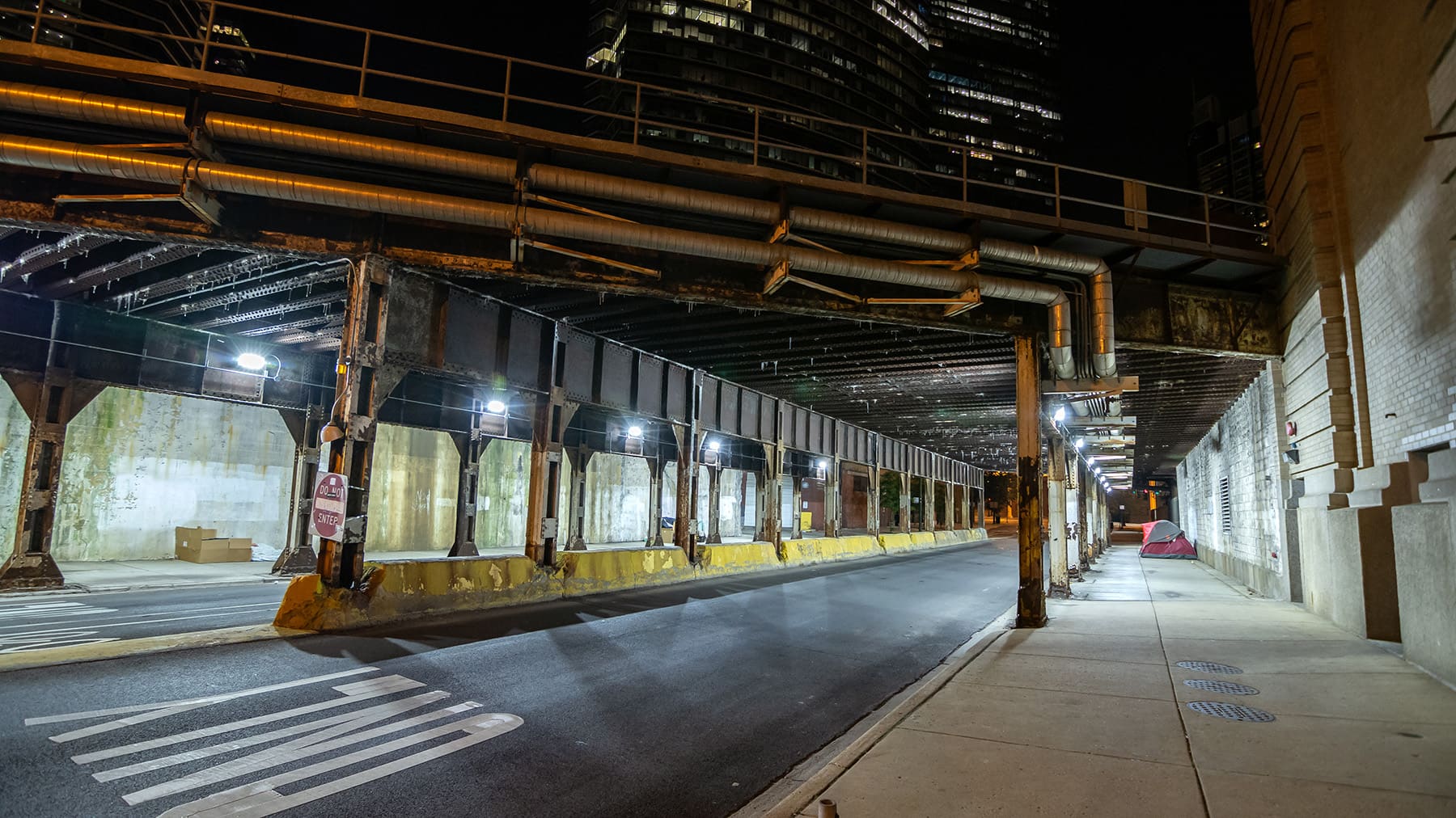 Dark Chicago city alley industrial train bridge underpass with homeless tents and boxes at night