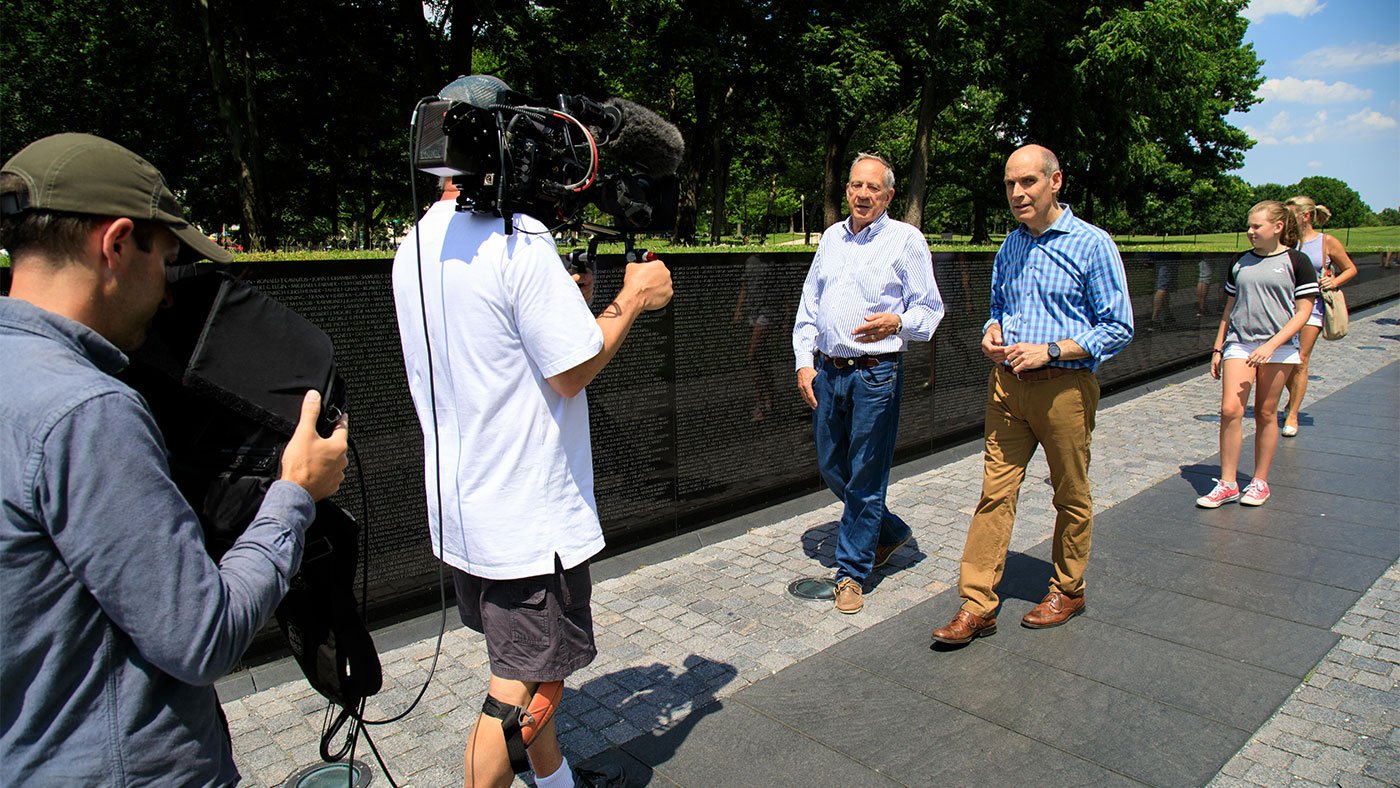 Director of Photography Tim Boyd and Series Producer Dan Protess look on as Geoffrey Baer interviews Jan Scruggs at the Vietnam Veterans Memorial in June 2017