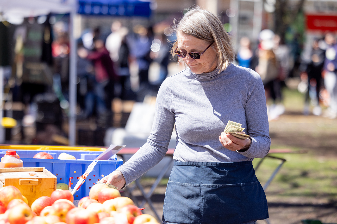 A woman holds cash while looking at apples