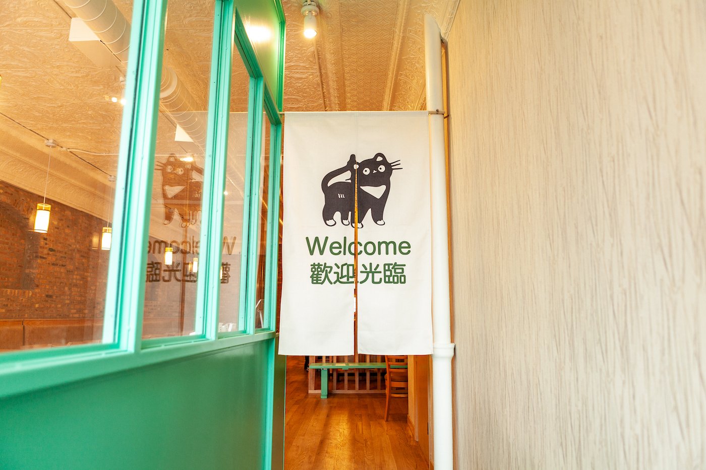 A cat logo on a partitioned curtain that says welcome in a restaurant entryway