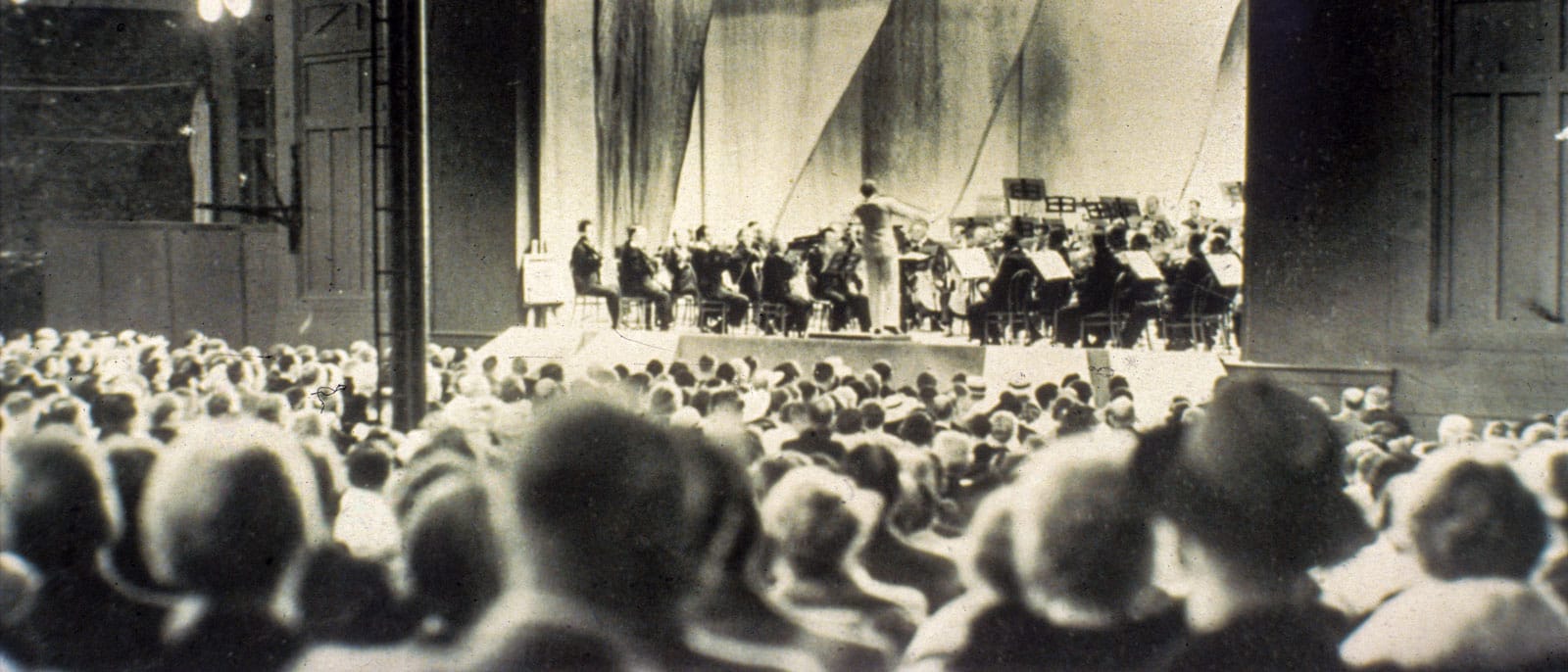 Vintage photo of a crowd of people watching an orchestral performance on stage
