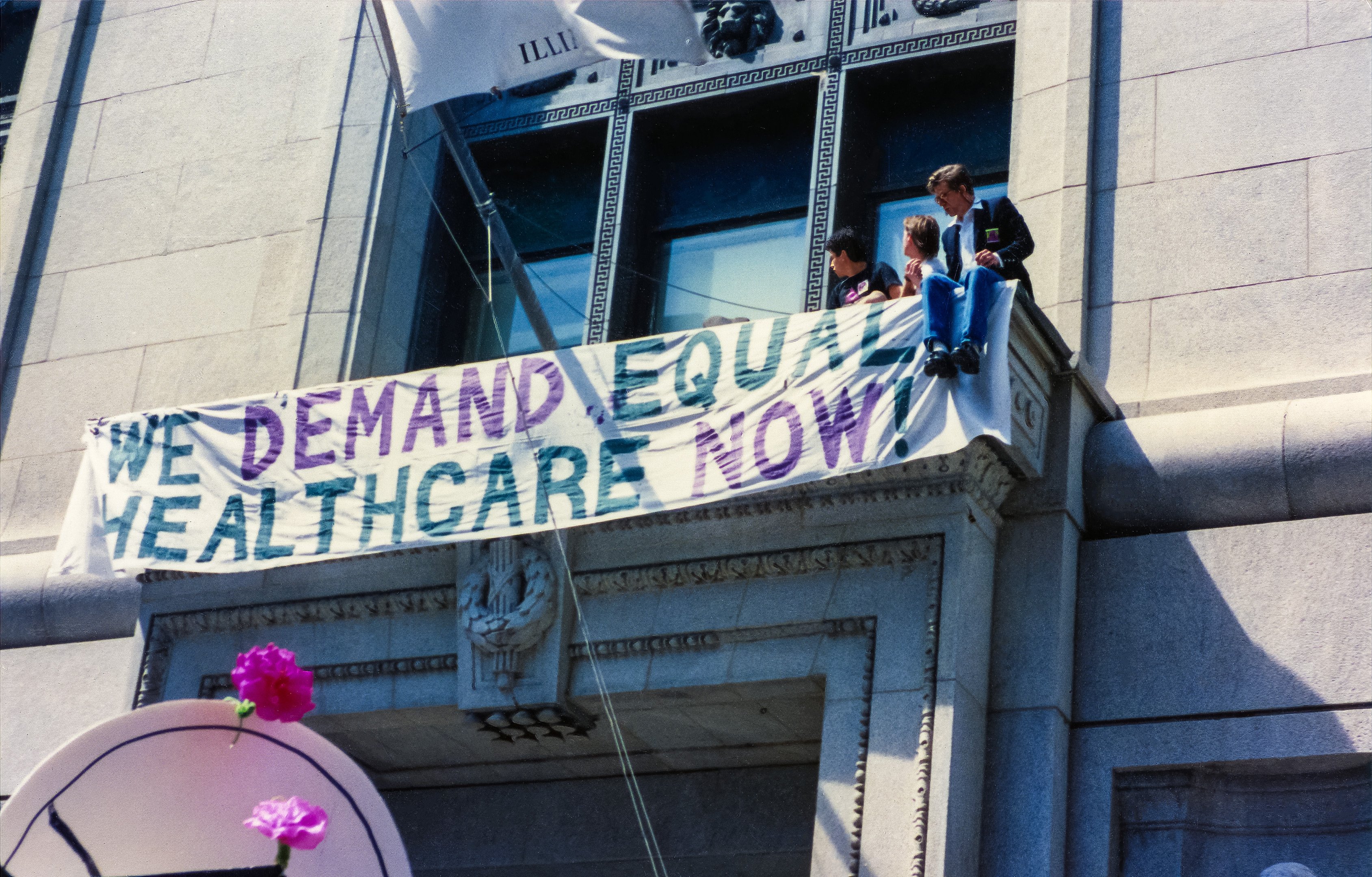 Danny Sotomayor, Bill McMillan, Tim Miller, Frank Sieple, and Paul Adams unfurled the “We Demand Equal Healthcare Now” banner outside a window at the County Building.