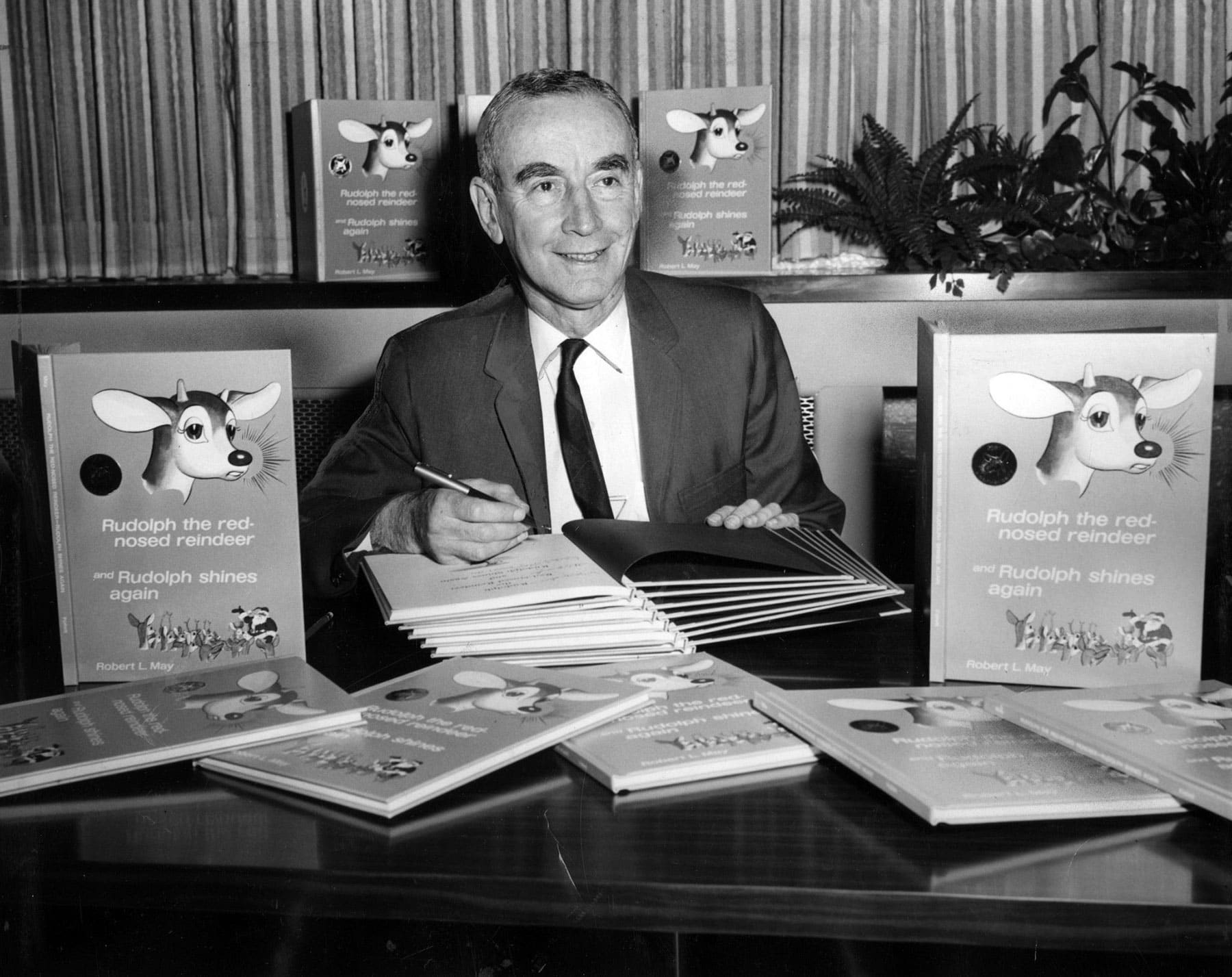 Robert Lewis May sitting behind his desk with copies of the Rudolph the Red-Nosed Reindeer books standing up.