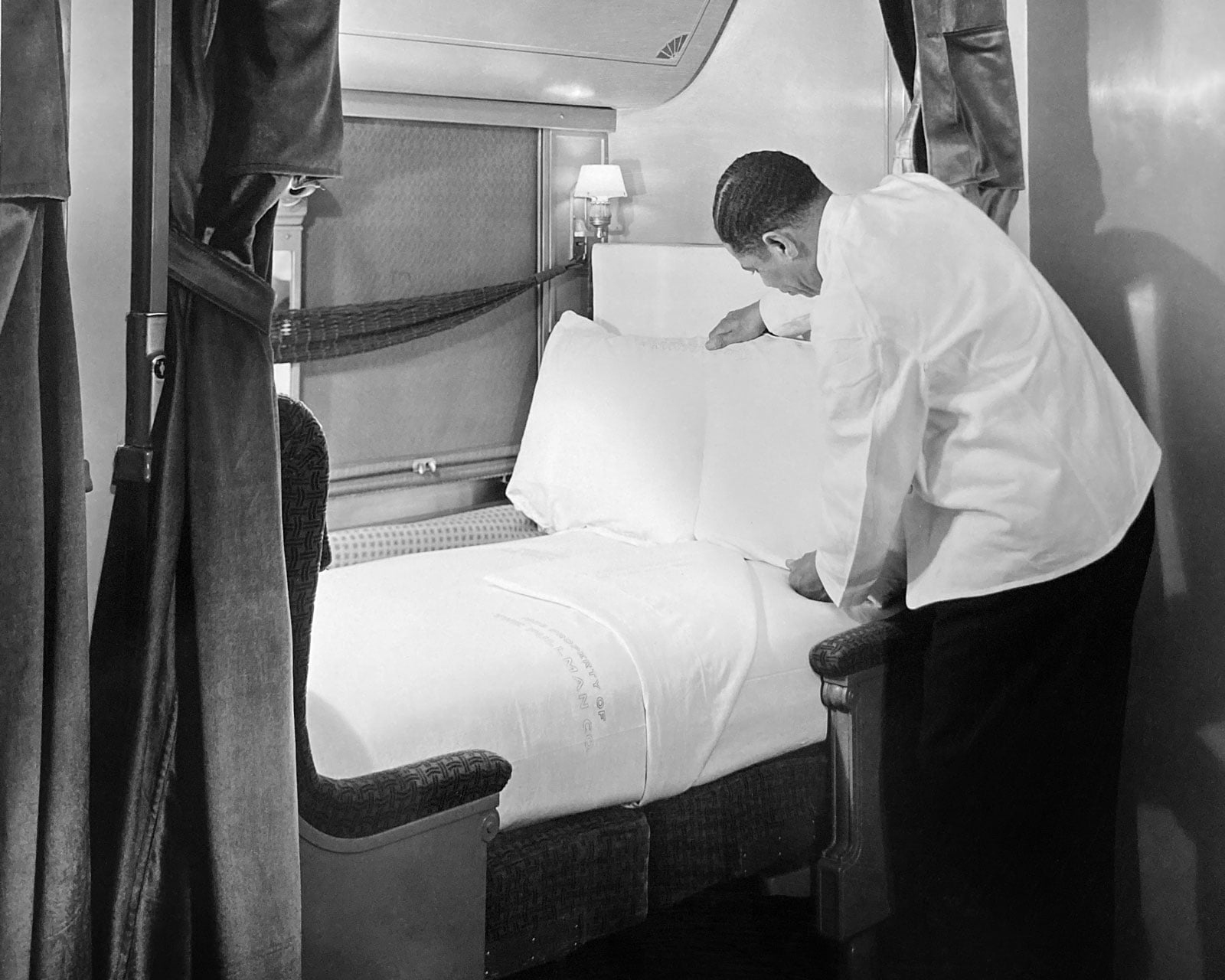 Porter adjusting pillow on bed in train car