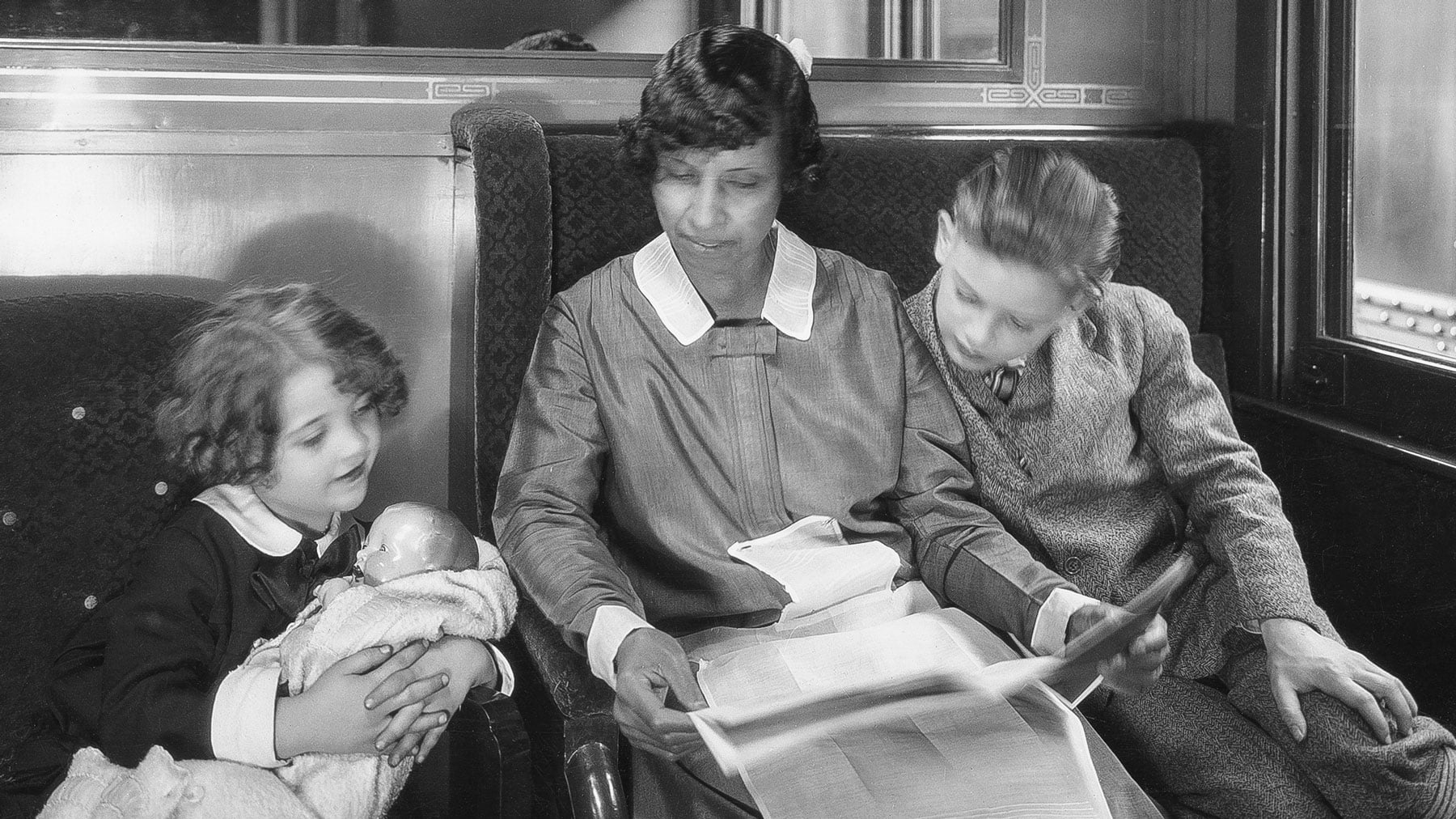 Black woman reading book to two children on train