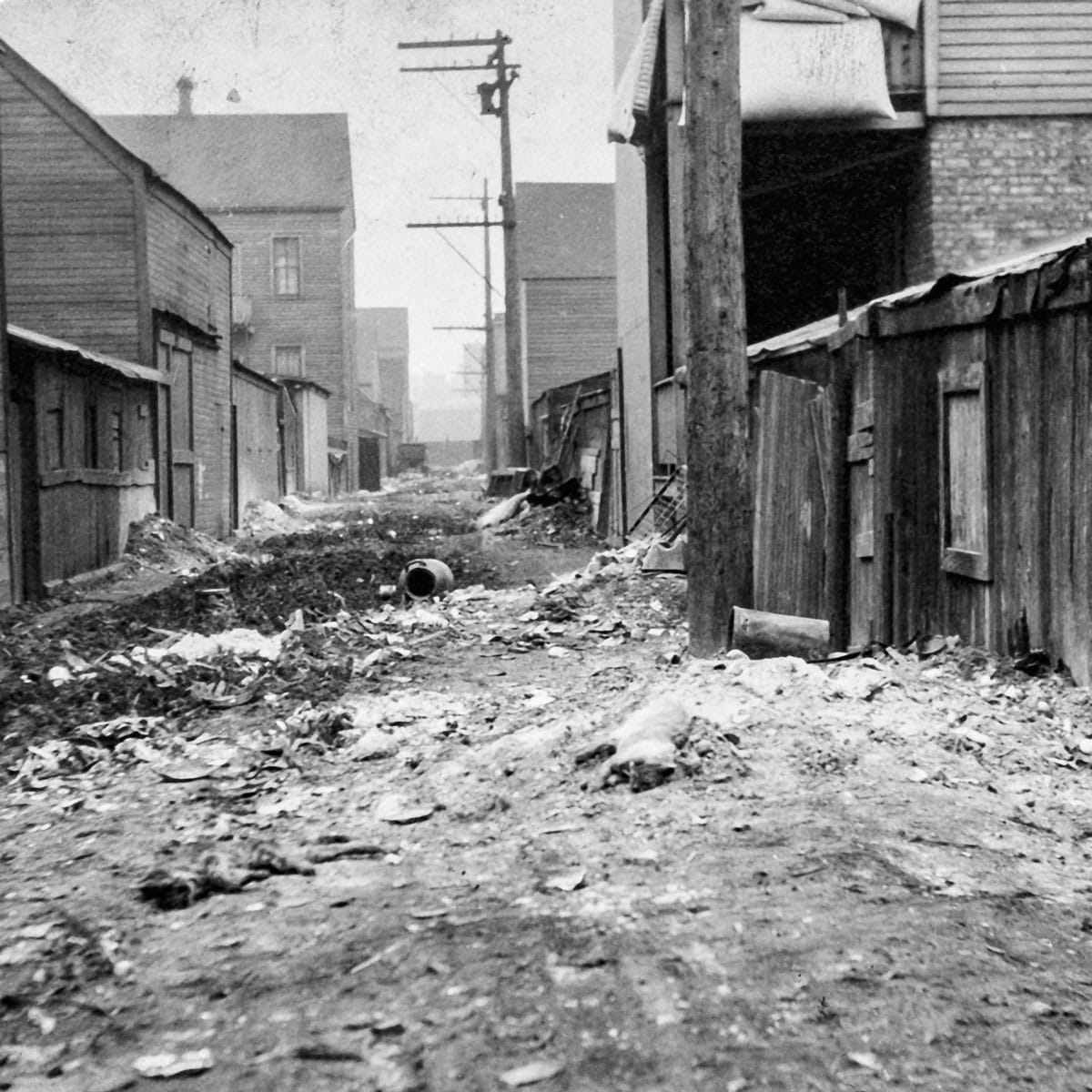 Vintage photo of an alley between buildings with trash and mud strewn about