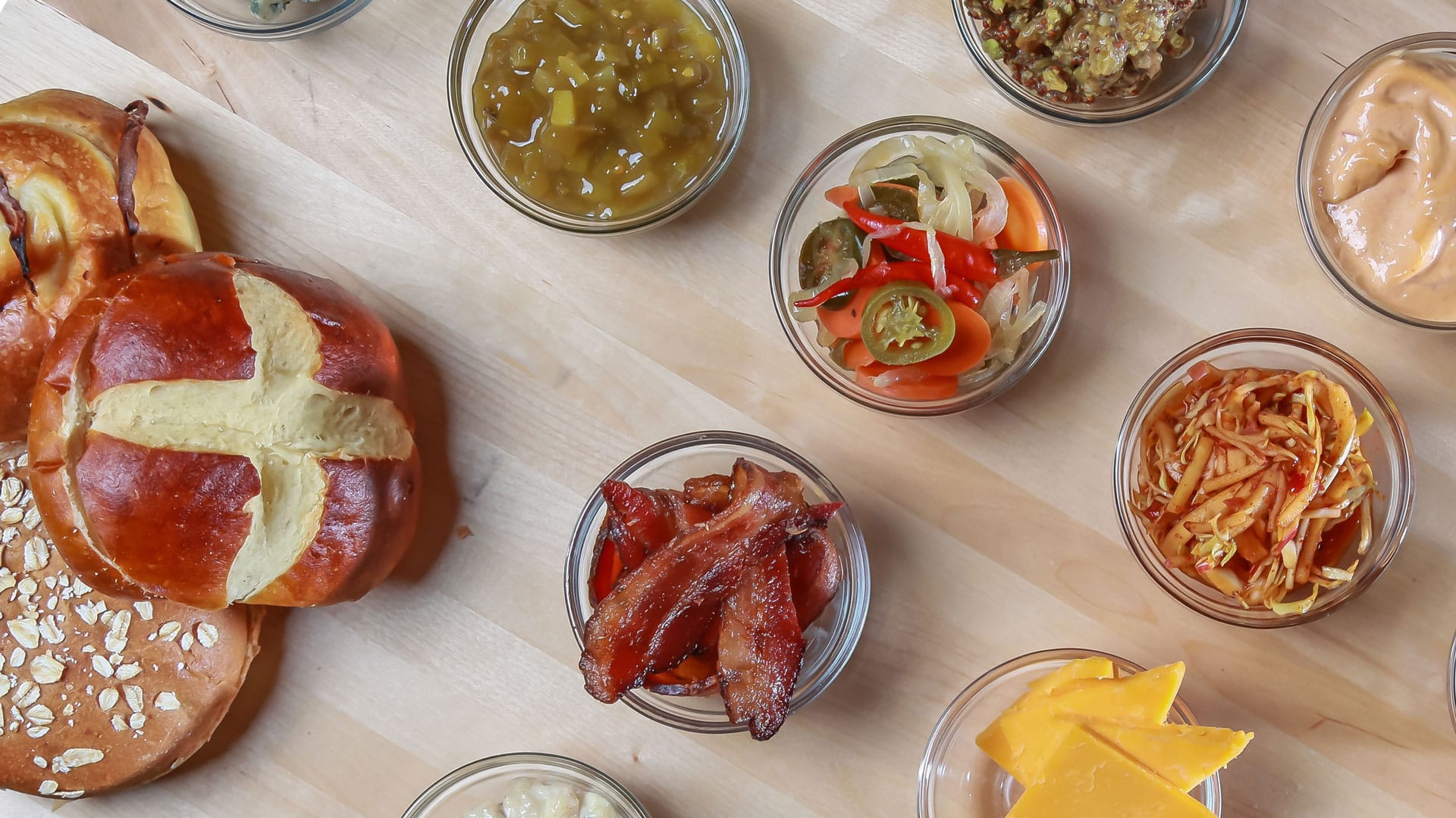 Buns and condiments arranged in bowls on a butcher block table surface