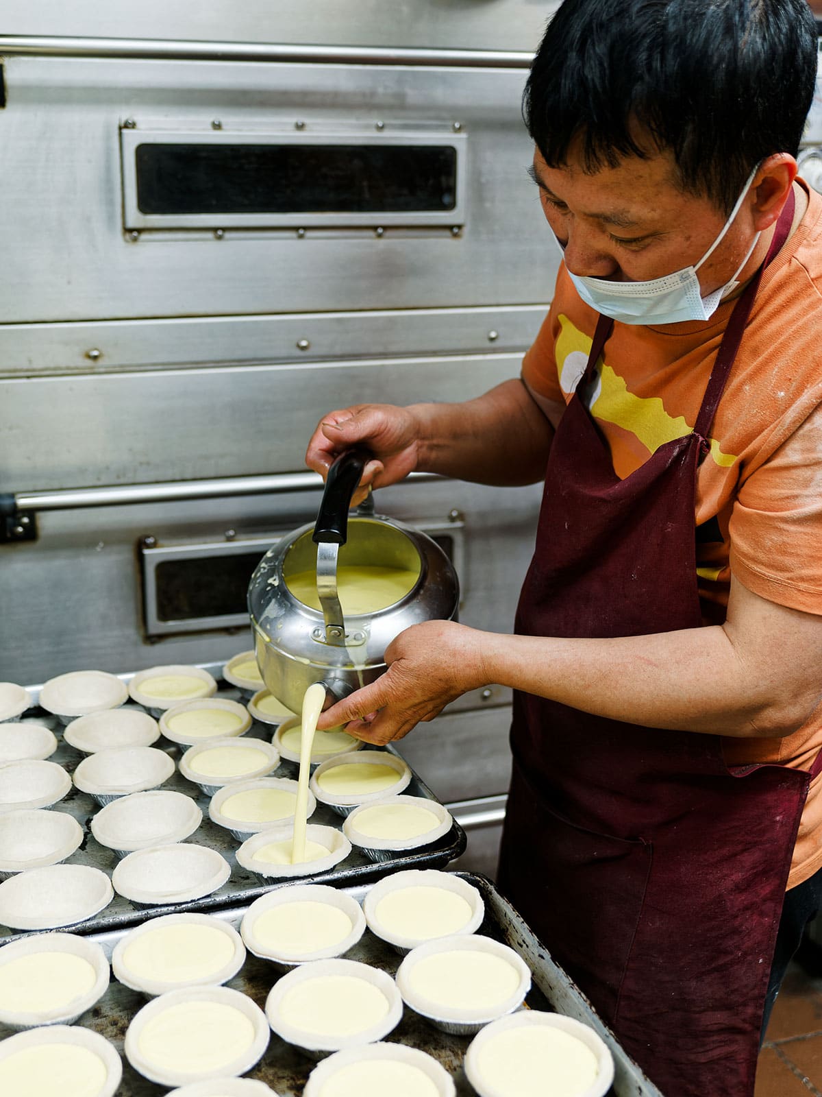 Man pouring filling into prepared dough in tins.