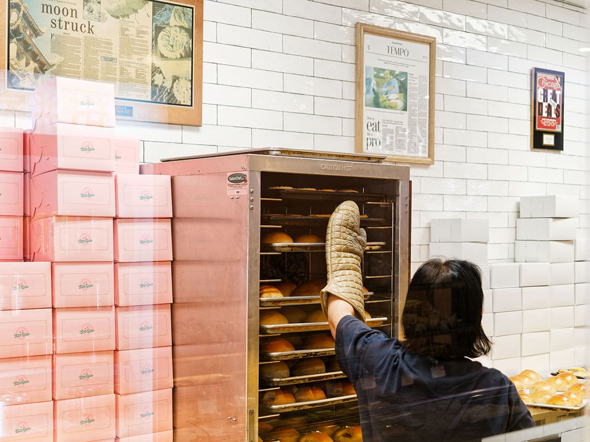 Baker pushes in tray of items into holding rack with stacks of boxes on the side.