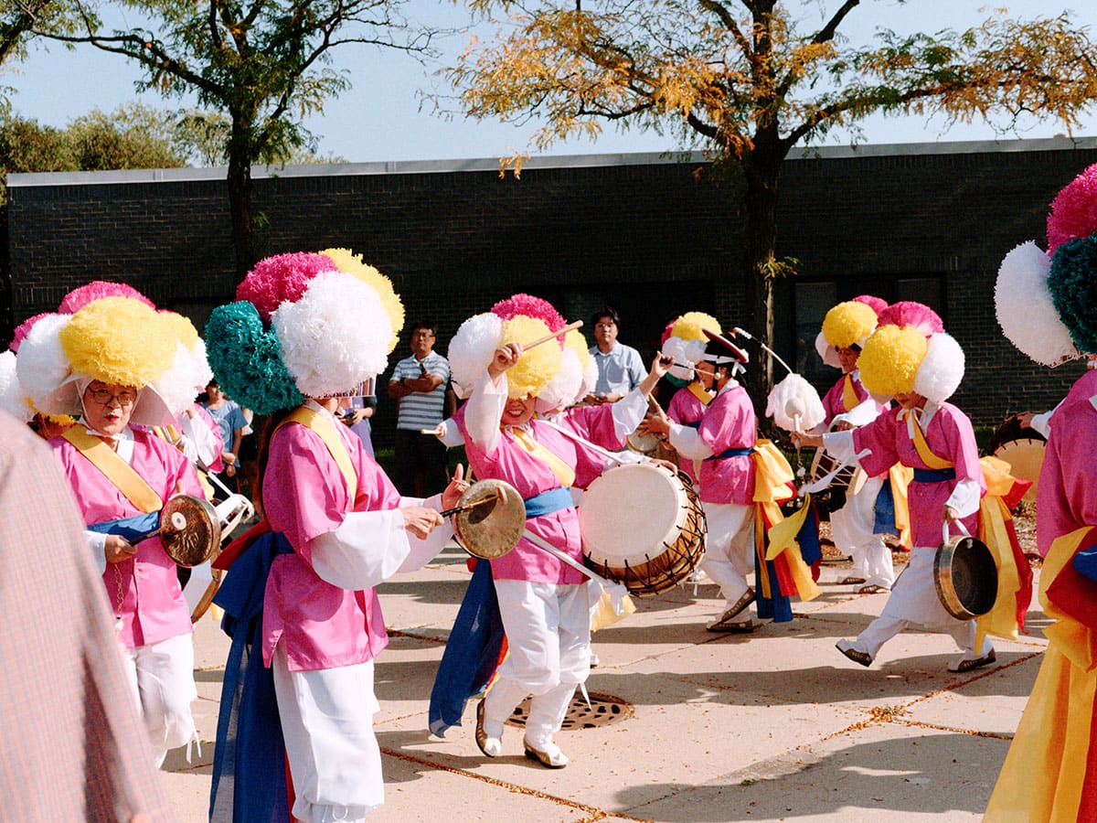 People wearing large puffy hats, pink tops and white pants play drums