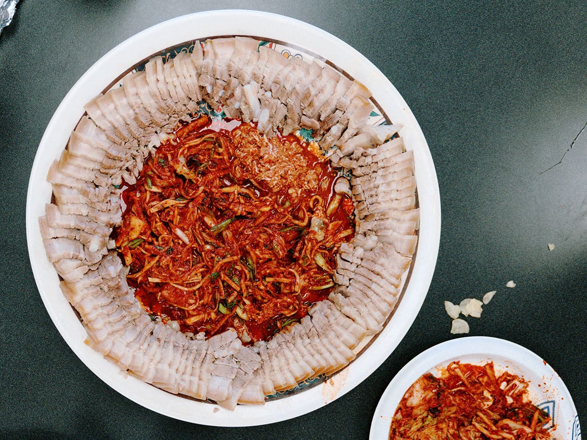 A round plate with sliced pork neatly arranged around the edge, with kimchi in the center
