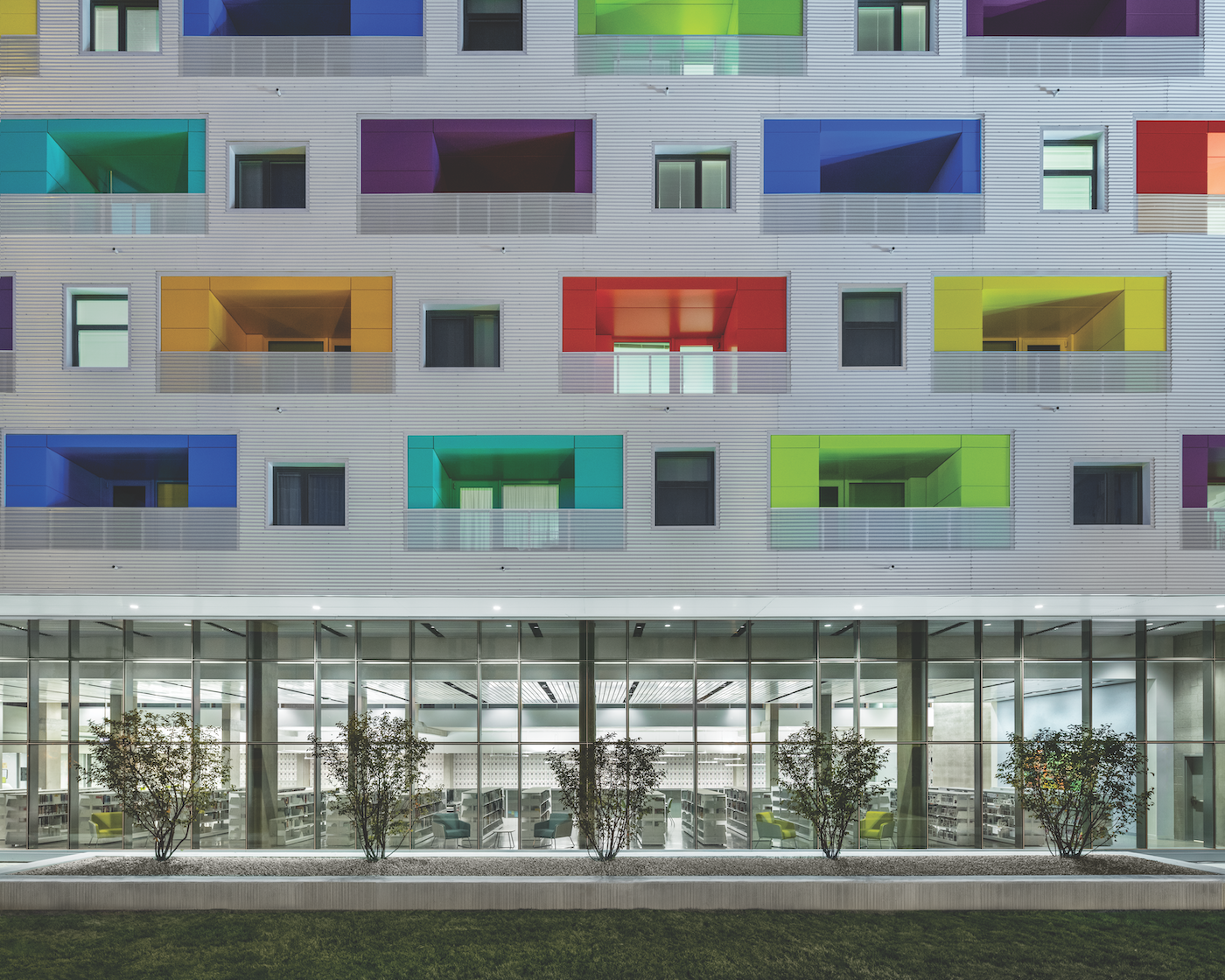 The colorful balconies of a building set into a gray facade over a view into a library underneath