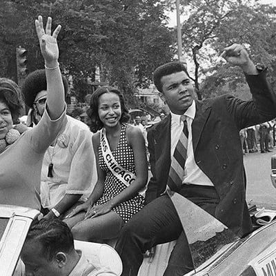 Muhammad Ali sitting in the back of a convertible waving to a crowd during the Bud Billiken Day Parade at 39th Street and Martin Luther King Drive, Chicago, Illinois on August 9, 1969. Photo: ST-40001287-0032, Chicago Sun-Times collection, Chicago History Museum