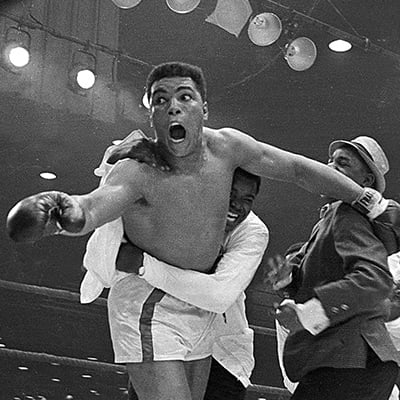 Cassius Clay's handlers hold him back after he is announced the new heavyweight champion of the world after knocking out Sonny Liston. Bundini Brown embraces Ali. Luis Sarria runs to the group in a smile on the right. Miami, Florida. February 25, 1965. Photo: Courtesy of AP Images