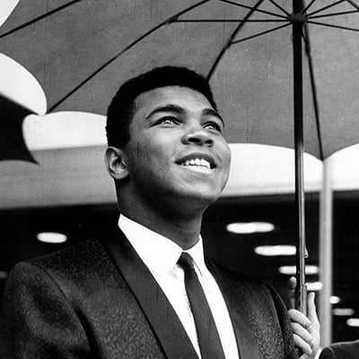 Muhammad Ali smiling as someone holds umbrella for him. He is in Frankfurt to have a title fight to Karl Mildenberger. Frankfurt, Germany. September 2, 1966. Photo: Courtesy of ZUMA Press, Inc./Alamy Live News