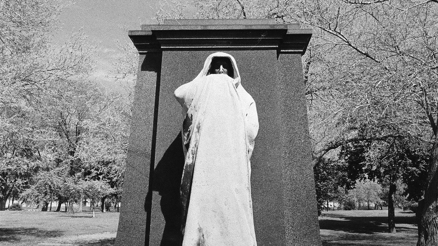 The Eternal Silence sculpture, pictured here in 1977. The black-and-white image shows a hooded sculpture set against a slab of black granite. Image: ST-40001541-0009, Chicago Sun-Times collection, Chicago History Museum