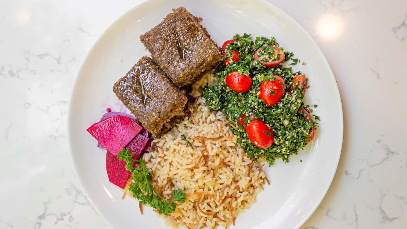 Kibbeh on a plate with rice, greens, and other vegetables. 