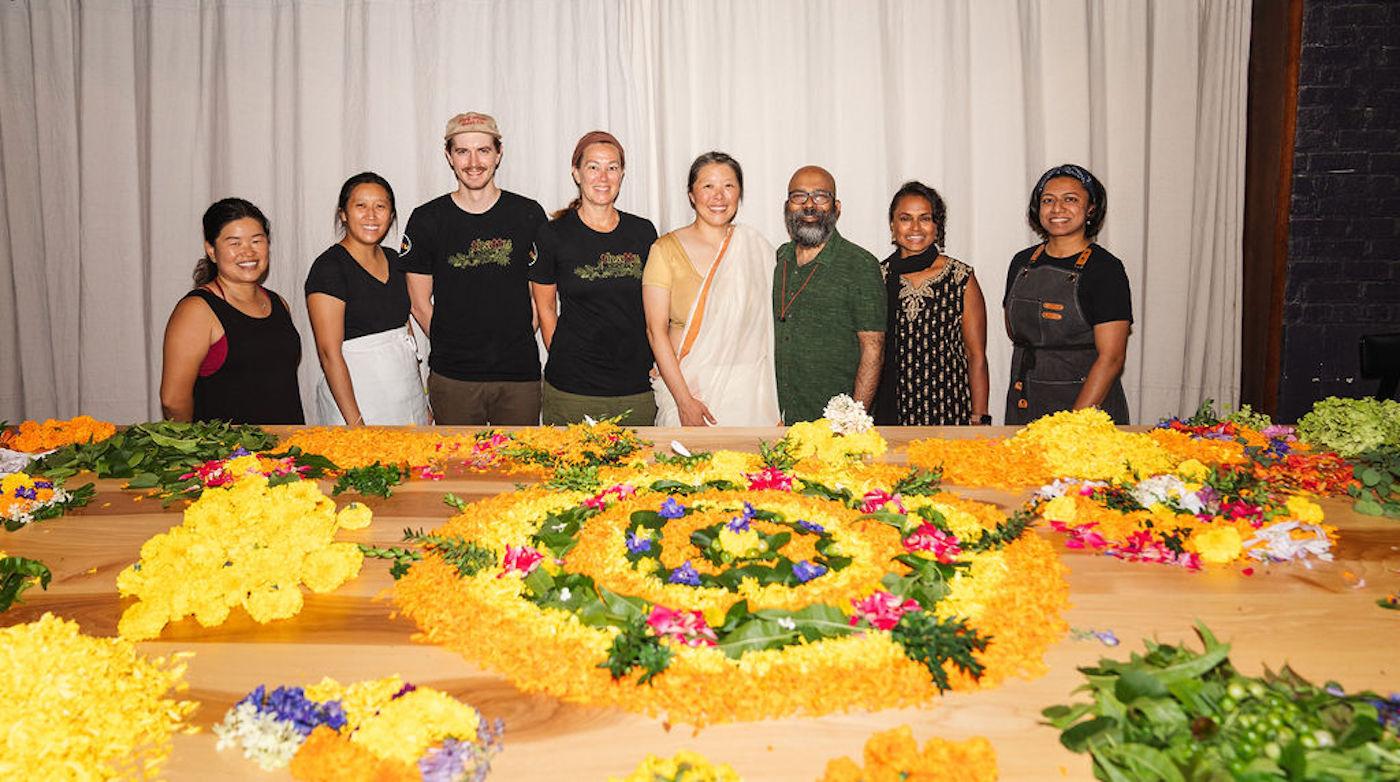 A group of people stands behind a table covered in traditional south Indian floral carpets