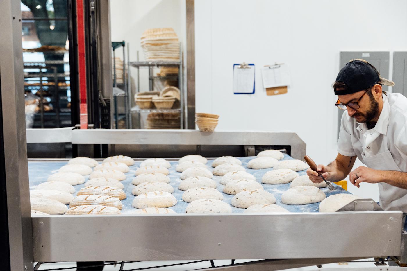 Ted Dreier scores loaves of bread on a conveyor belt waiting to go into an oven
