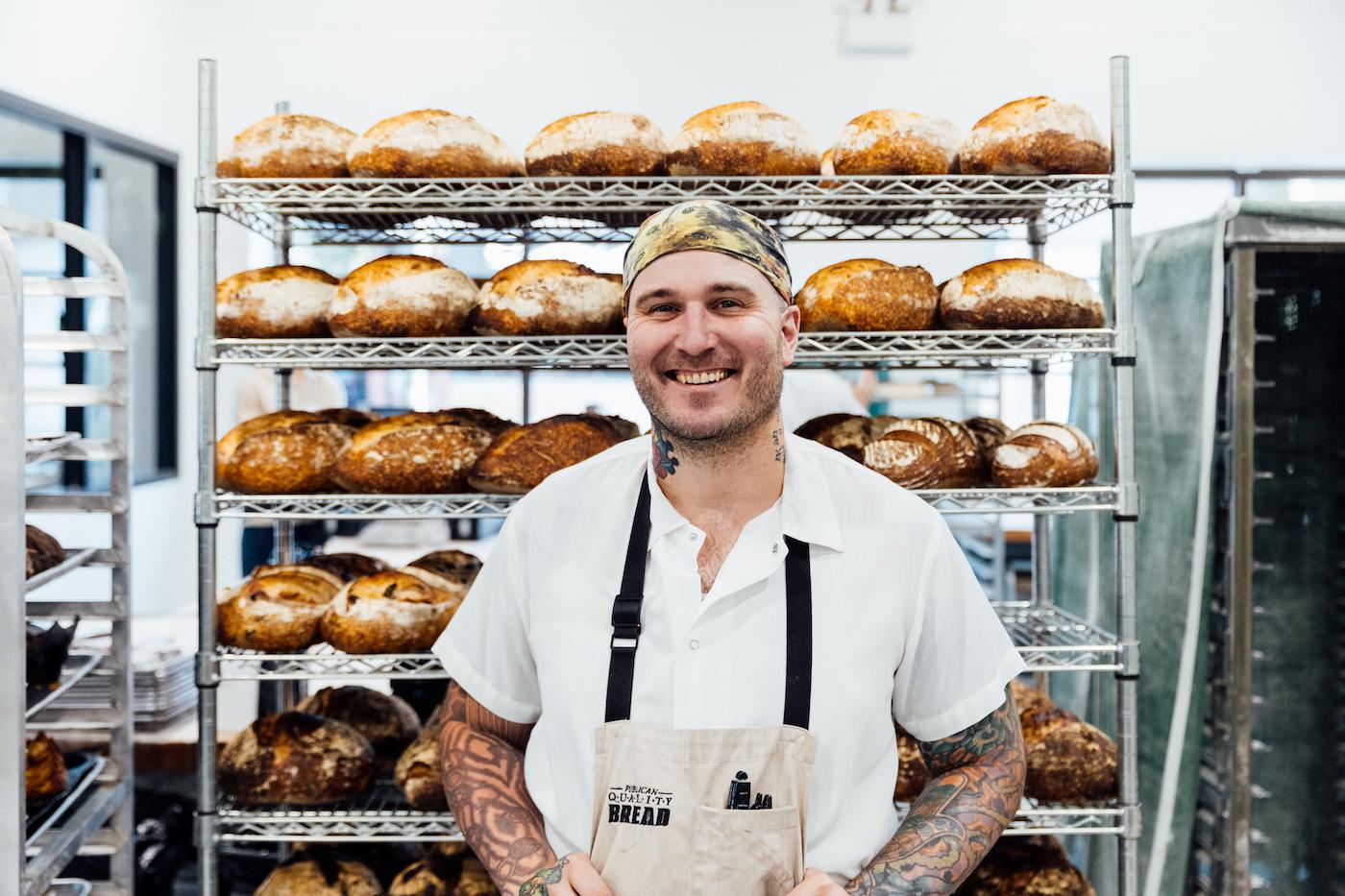 Greg Wade stands in front of a rack of cooling loaves of bread
