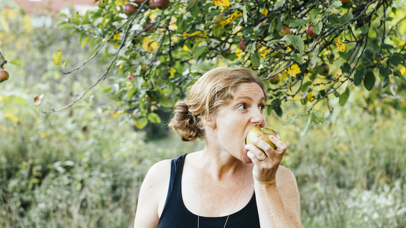 Abra Berens biting an apple under an apple tree