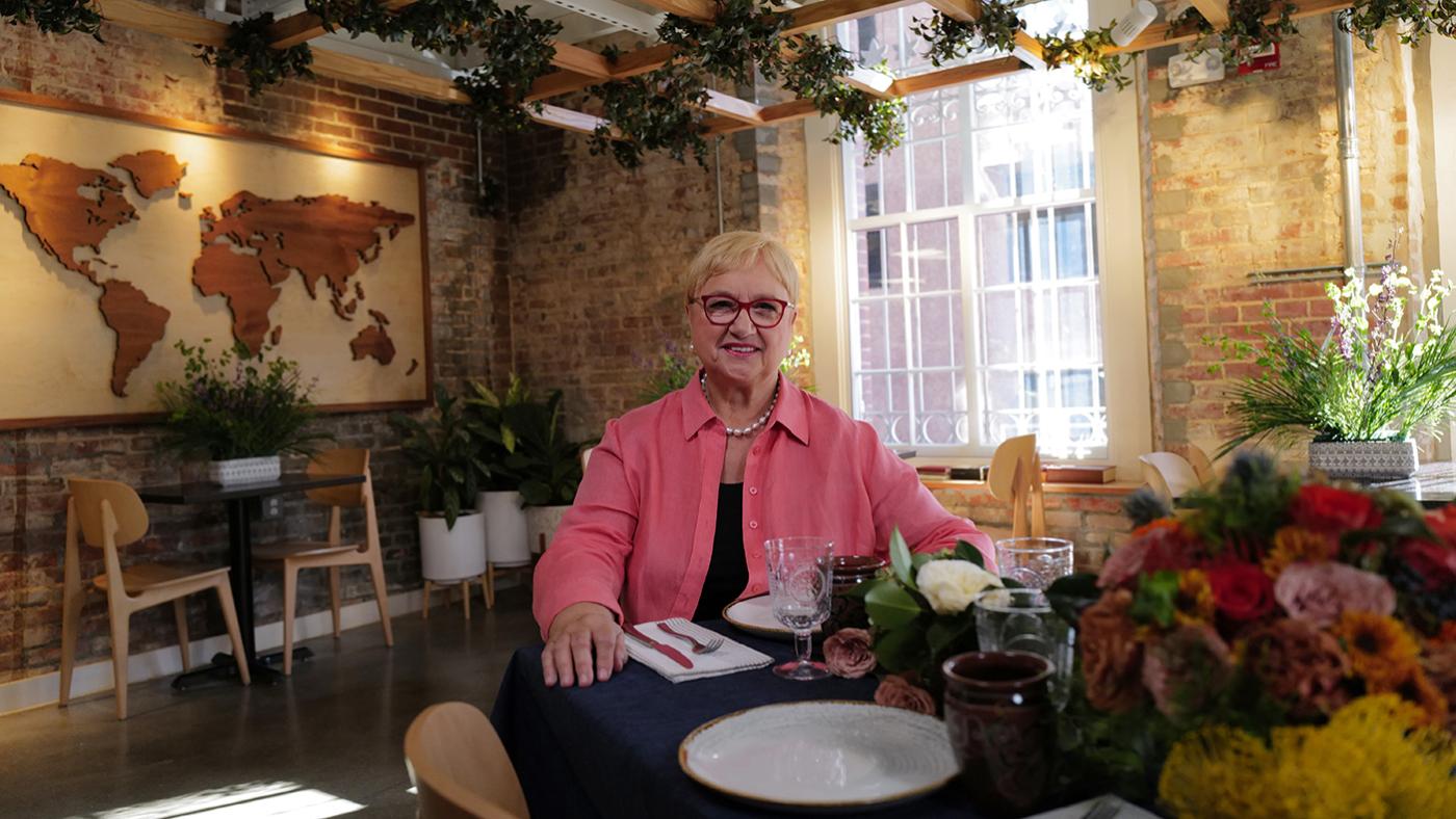 Lidia Bastianich sits at a set table near a map of the world