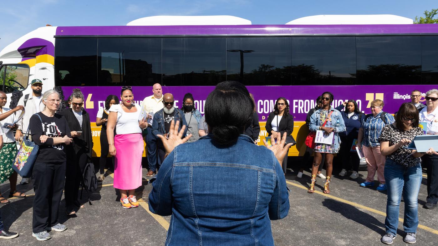 A group of people stand in front of a bus while Chicago's Chief Equity Officer Candace Moore addresses them