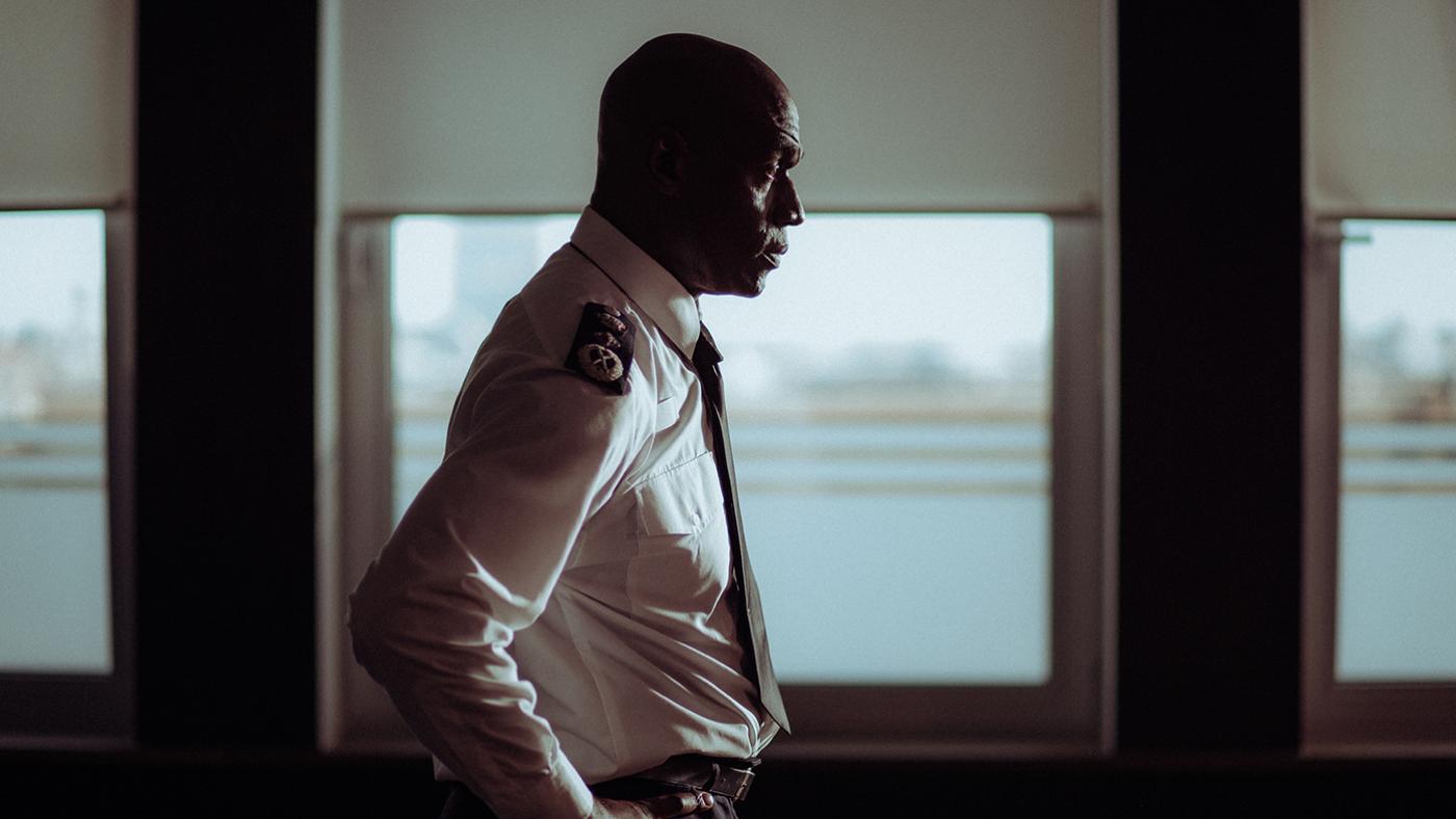 Leonard Kane stands in his police uniform in profile in front of a window