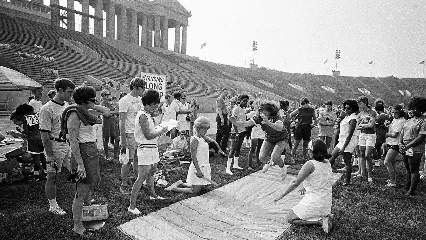 A black and white image showing a group of people surrounding a long jumper at Soldier Field.