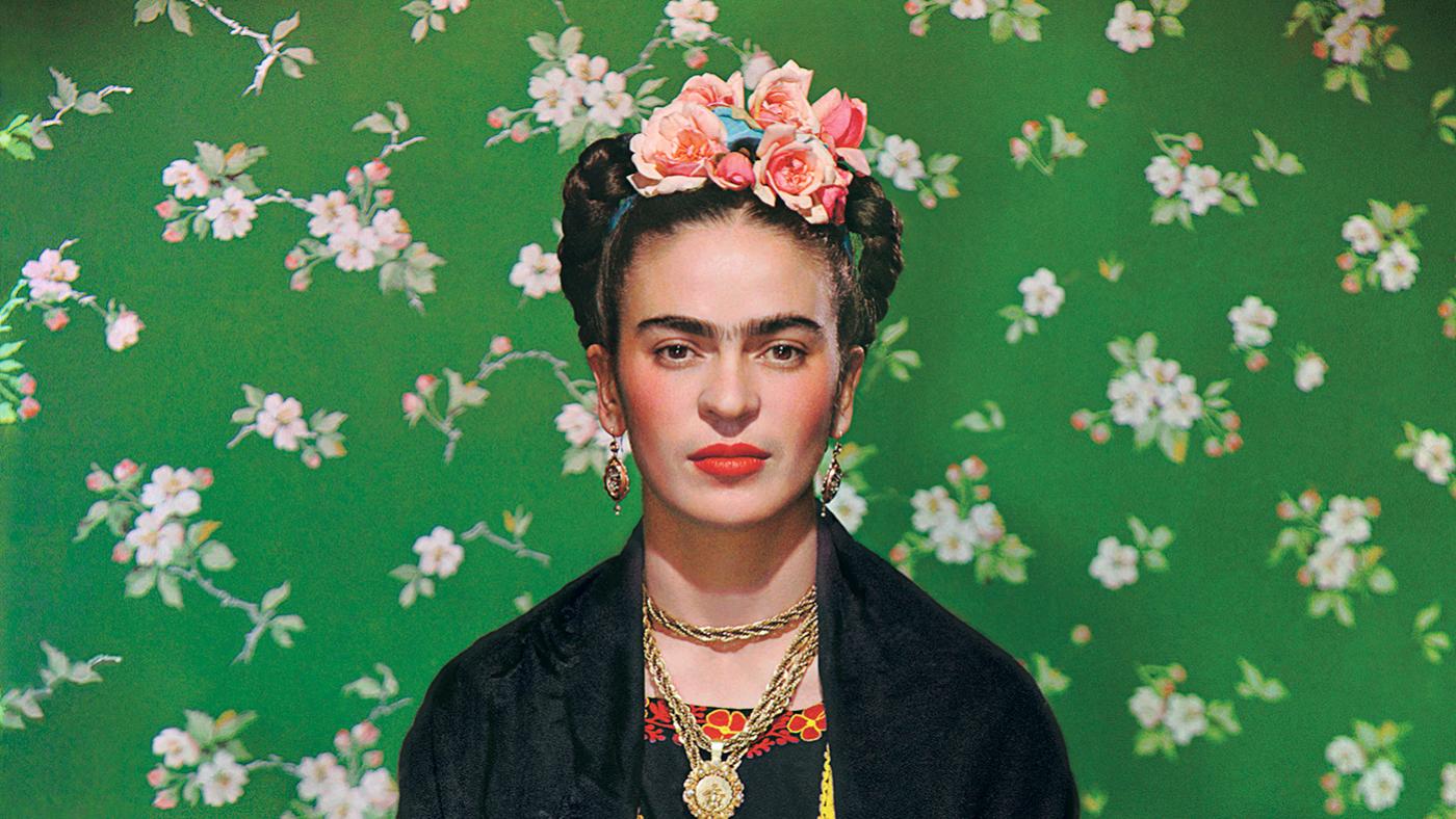 Frida Kahlo against a green backdrop with flowers in her hair