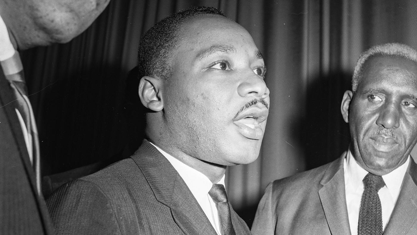 Martin Luther King, Jr. in between two men in a black and white photo from 1963