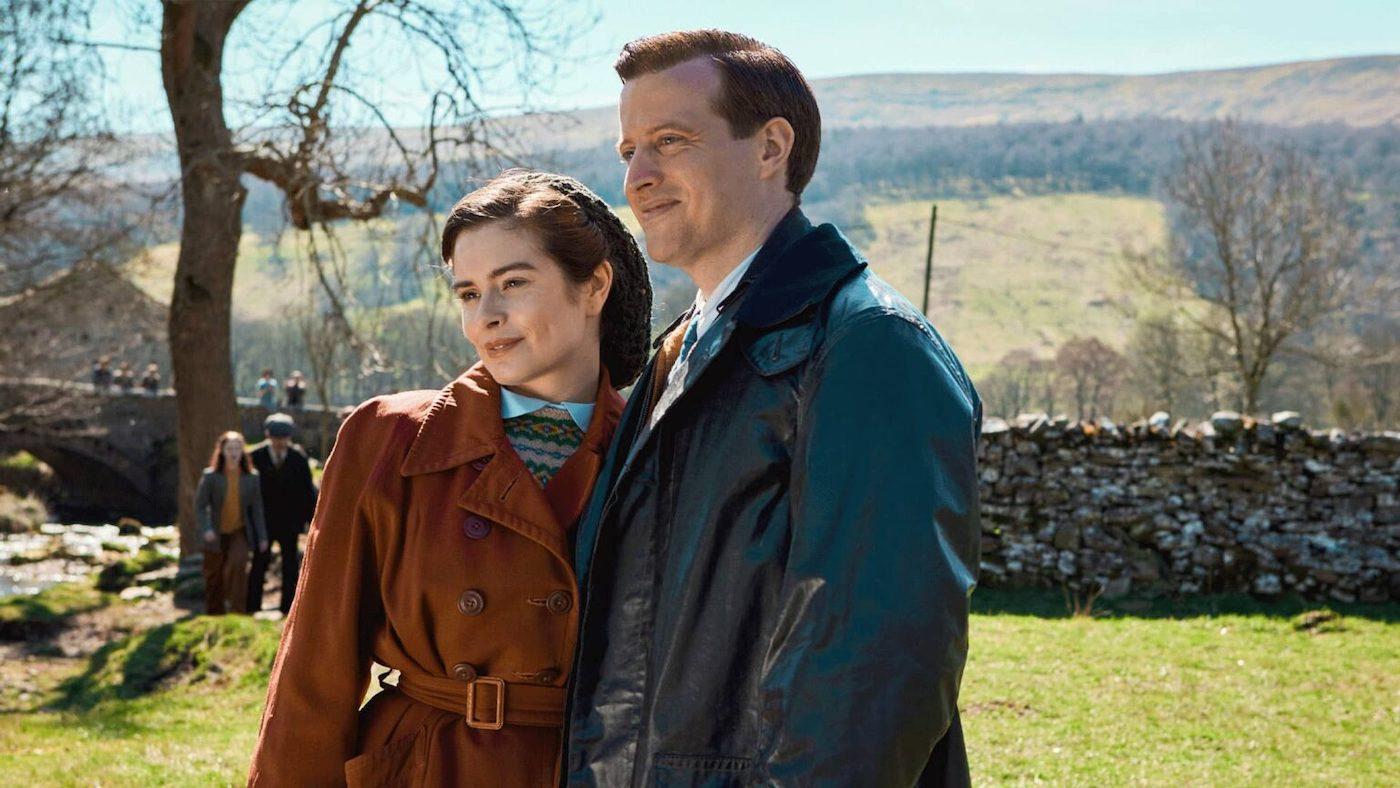 Helen and James stand next to each other in coats on a farm