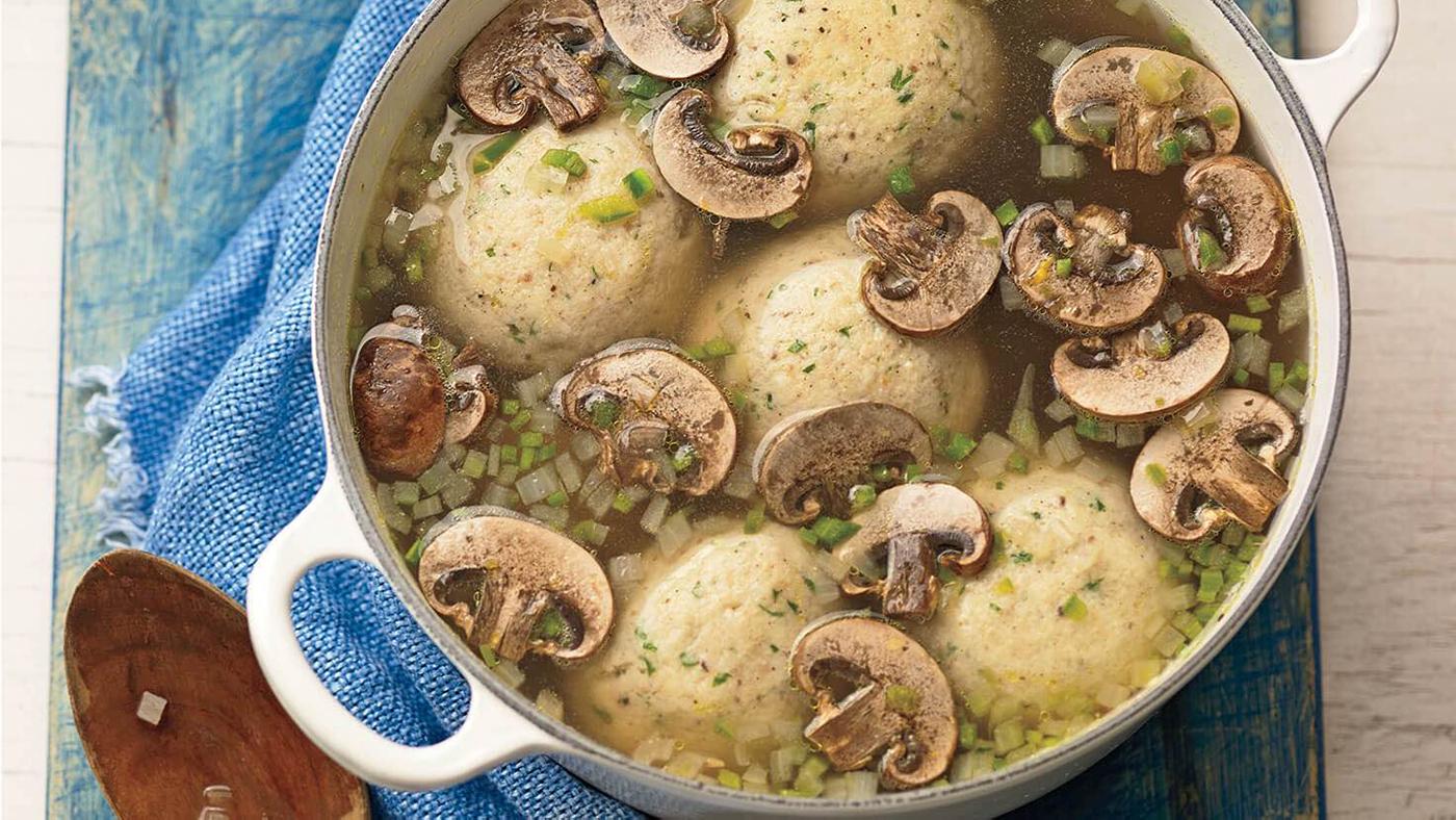 A pot of mushroom jalapeno matzo ball soup seen from above, with a wooden spoon to the side