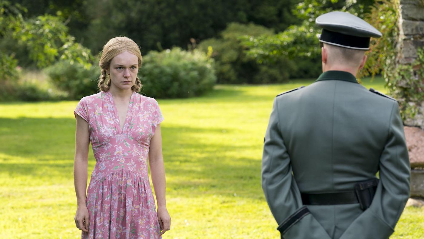 Marga stands on a lawn in a pink dress and looks uncertainly at a German officer eying her