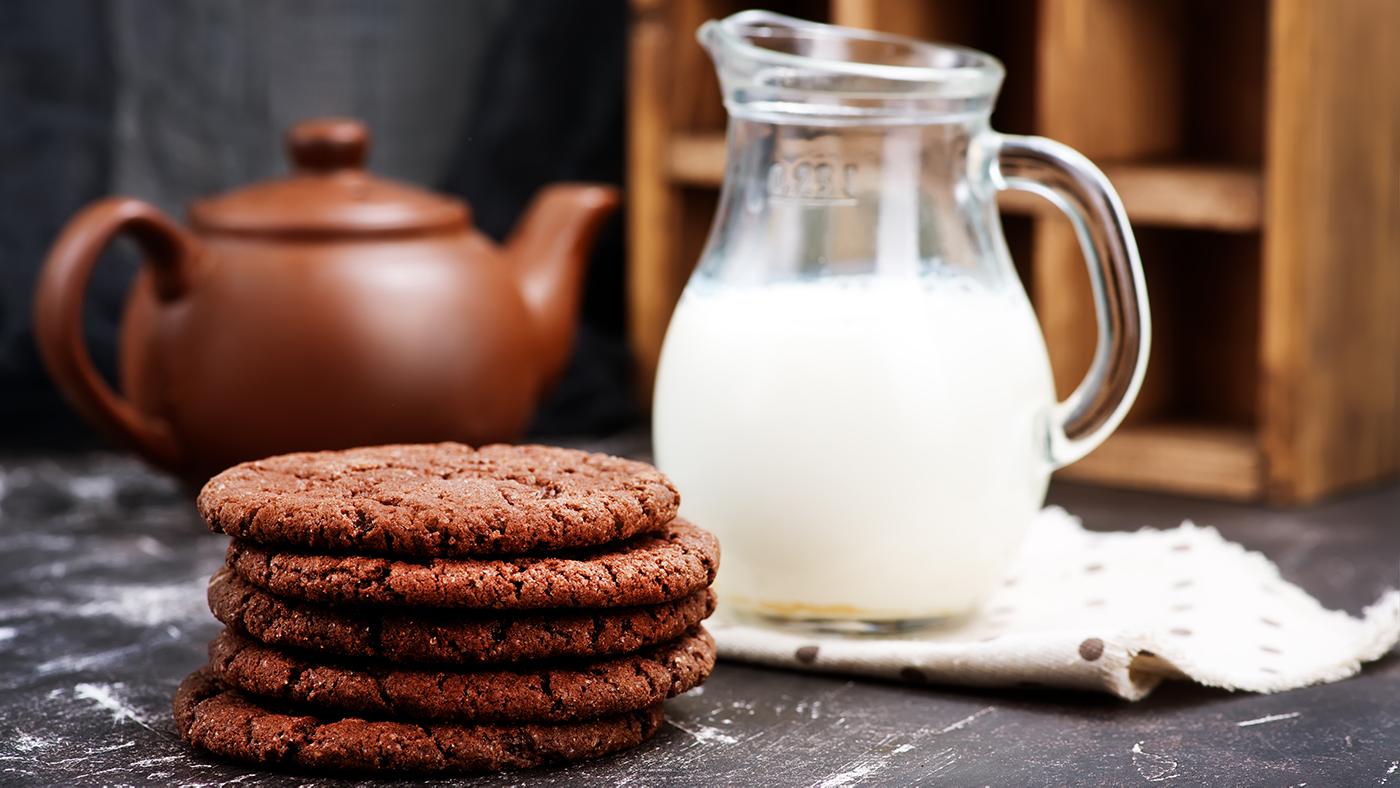 A stack of chocolate ginger molasses cookies sits near a jug of milk