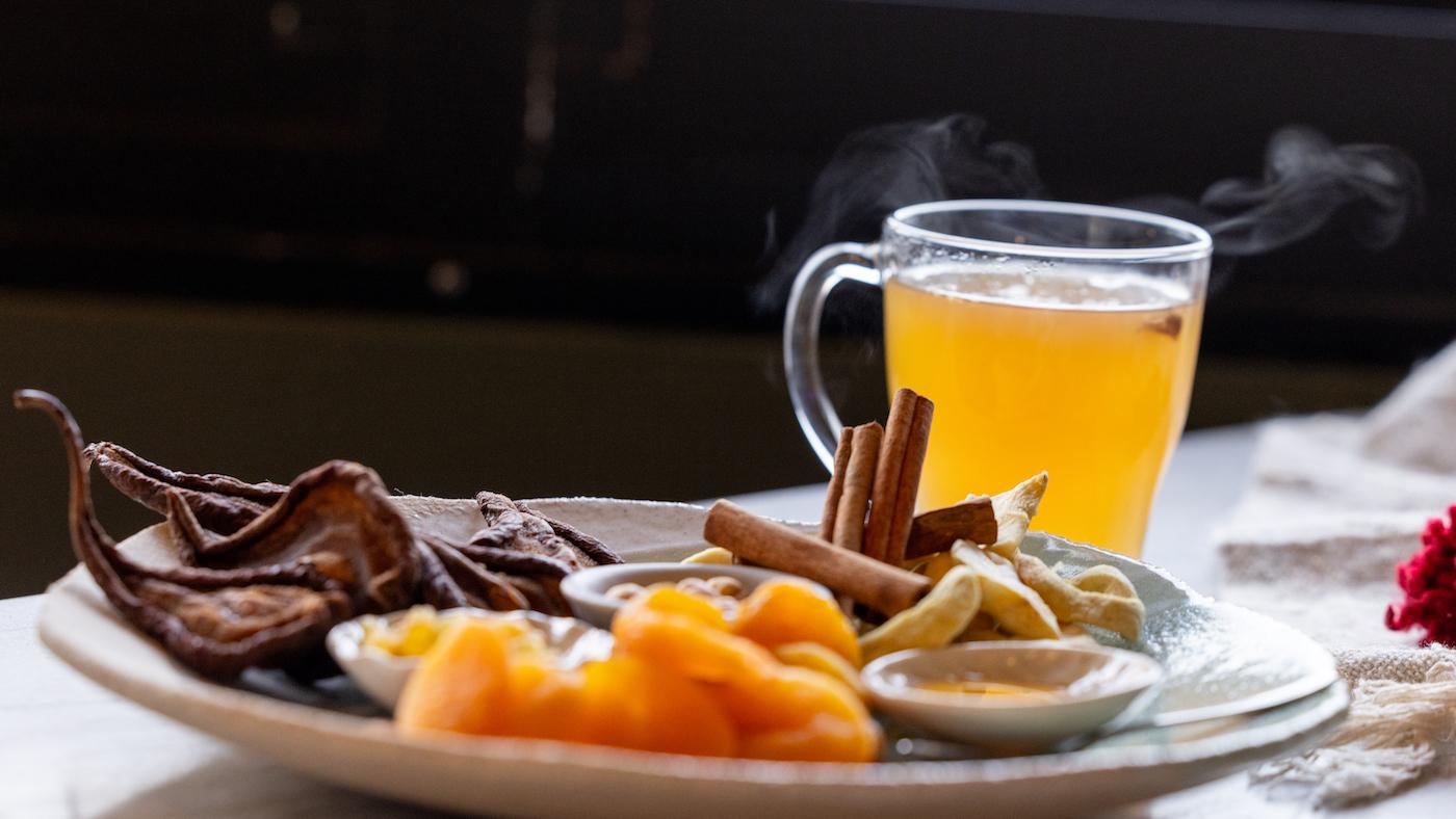 A steaming mug of cider behind a plate of its ingredients