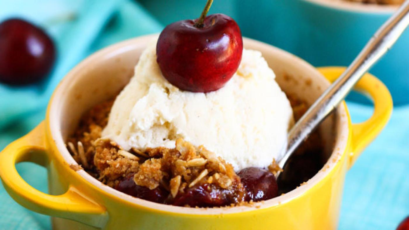 A yellow mug of cherry crumble topped with ice cream and a cherry